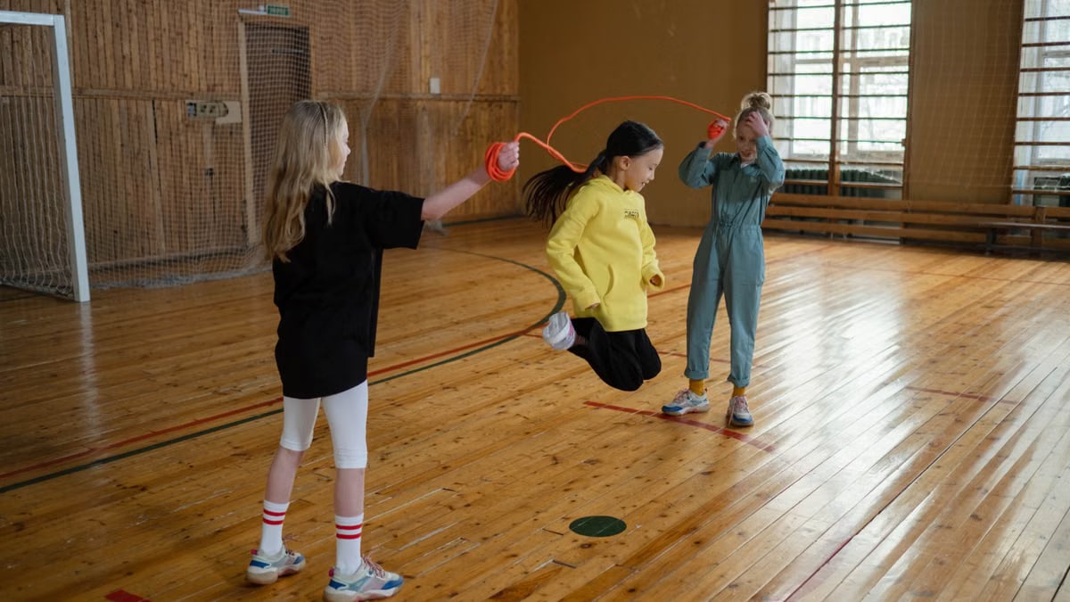 Three children enjoying a fun jump rope activity in a wooden gym.